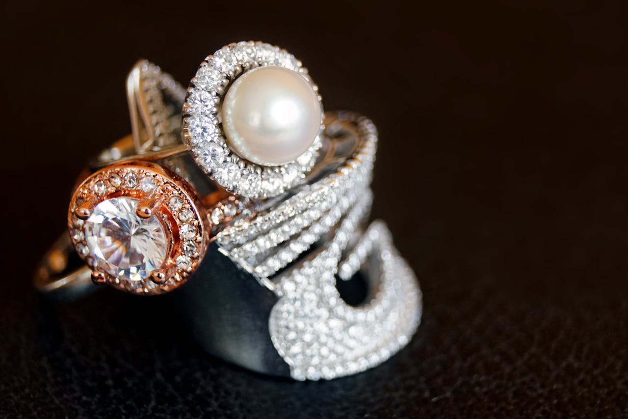 services-02 Close-up of luxurious pearl and diamond rings with gold accents on a black background.