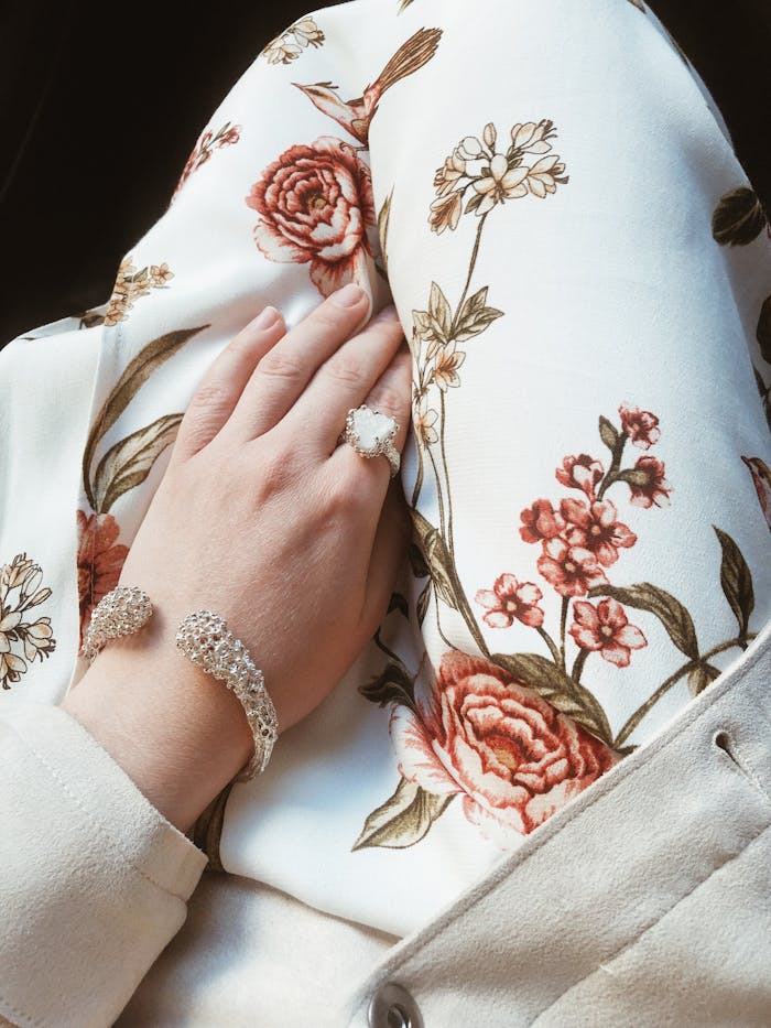Stylish hand adorned with jewelry on floral fabric, showcasing an elegant fashion statement.