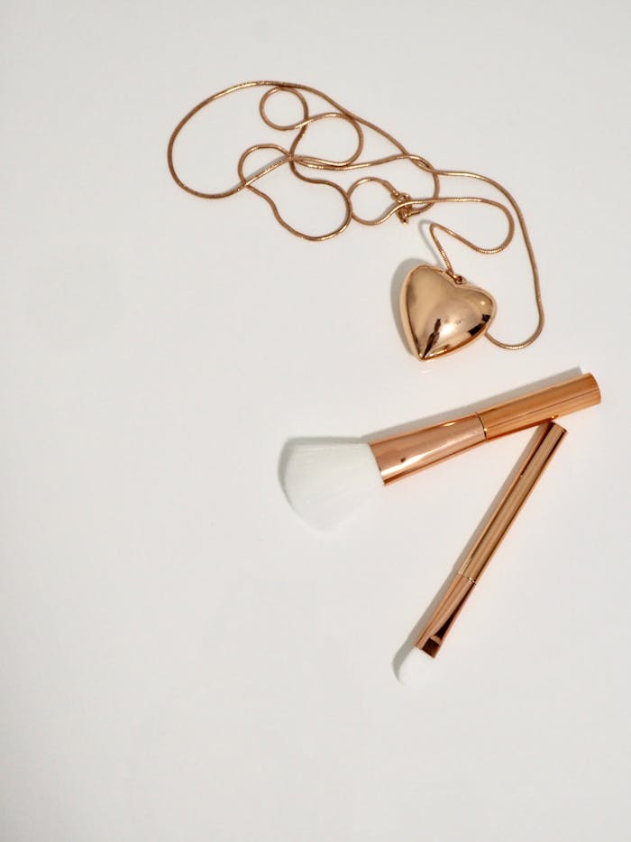 services-bg A charming flat lay of a heart-shaped pendant and makeup brushes on a white background, creating a minimalist still life.