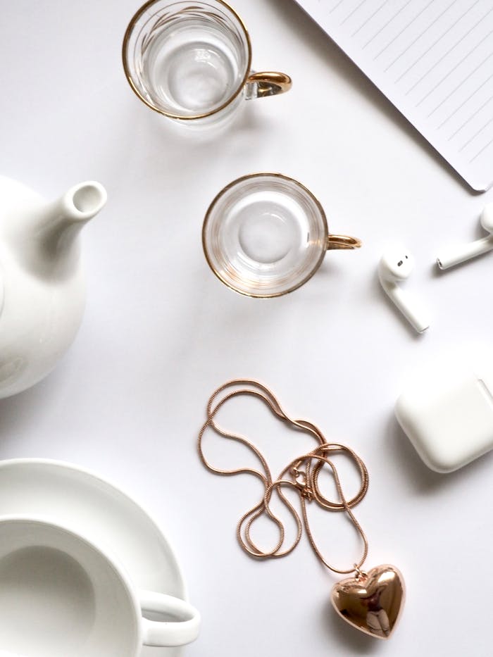 Minimalist flat lay featuring gold jewelry, glass cups, and a white tea set, perfect for luxury lifestyle themes.