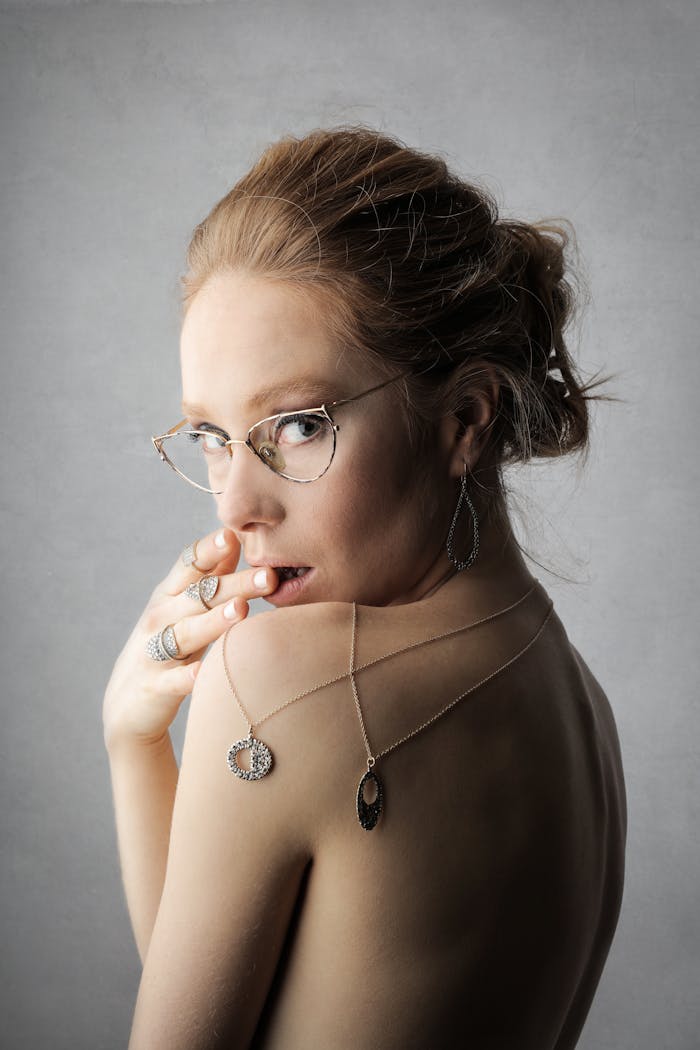 Stylish woman with glasses and jewelry posing in studio setting.